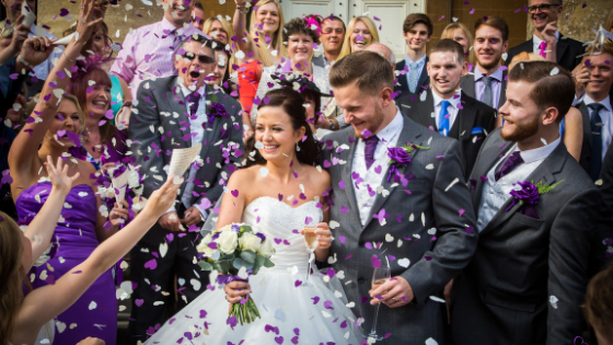 A smiling bride and groom are showered in confetti outside Leigh Court