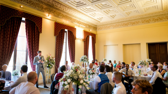 A groom is giving a speech in a large yellow room at his Leigh Court wedding