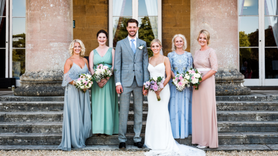 A bride and groom pose with bridesmaids on the steps outside Leigh Court